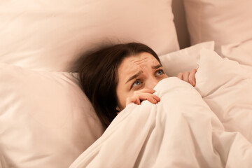 Upset young woman lying in bed at home, closeup