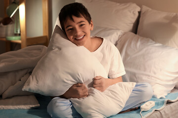 Little boy with pillow sitting on electric heating pad in bedroom at night