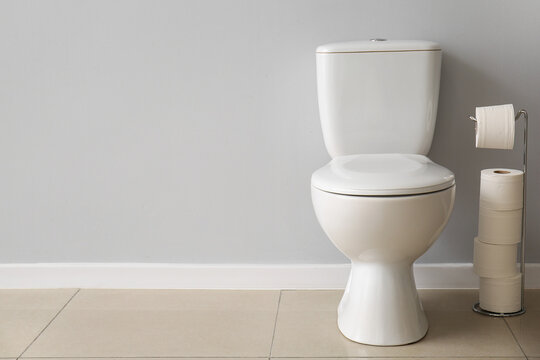 Ceramic toilet bowl and holder with paper rolls near grey wall
