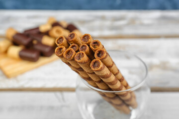 Glass with delicious rolled wafer cookies on light table, closeup