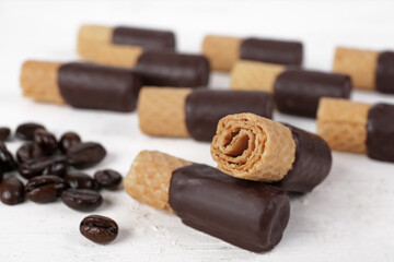Delicious wafer rolls and coffee beans on light table, closeup