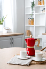 Wicker coaster with geyser coffee maker and cups on table in kitchen
