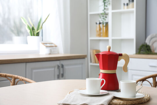Wicker coaster with geyser coffee maker and cups on table in kitchen