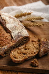 Board with loaf of fresh rye bread and wheat ears on wooden background
