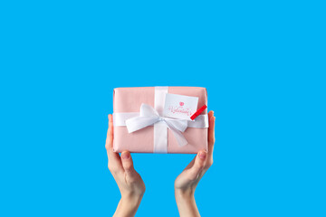 Female hands holding gift on blue background. Valentine's Day celebration
