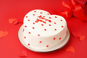 Plate with heart-shaped bento cake and gift on red background. Valentine's Day celebration