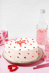 Plate with heart-shaped bento cake, gift, bottle and glass of tasty drink on pink background. Valentine's Day celebration