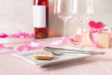 White plate with cutlery and heart-shaped cookie on pink tile table. Valentine's Day celebration