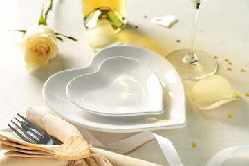 Heart-shaped plates, rose flower and cutlery in napkin on white table. Valentine's Day celebration
