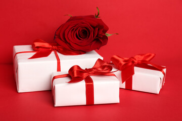 Gift boxes with beautiful bows and rose flower on red background. Valentine's Day celebration