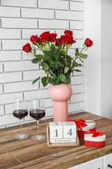 Calendar with date 14 FEBRUARY, gifts, wine glasses and roses on counter in kitchen