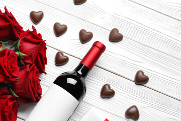 Bottle of wine, chocolate candies and rose flowers on white wooden background. Valentine's Day celebration