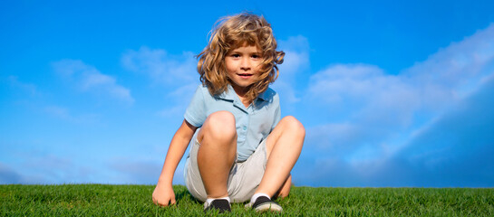 Portrait of a smiling little boy on green grass. Smiling boy having fun outdoor in spring garden. Spring and kid. Wide photo banner for website header.