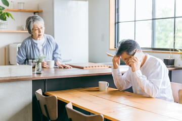 家でスマホで電話しながら困る高齢者男性(故障・修理・詐欺・悩む)