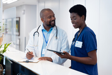 Fototapeta premium Smiling african american male and female doctor with tablet talking in hospital corridor