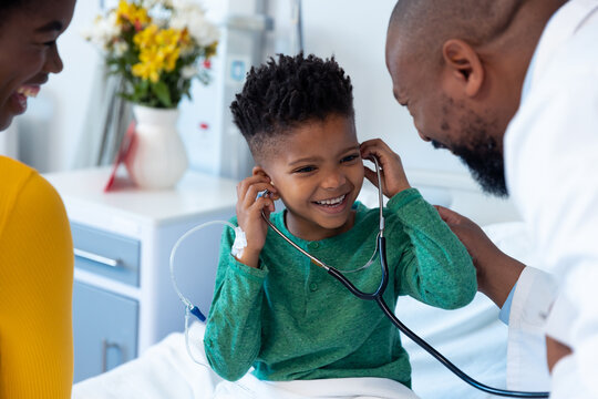 Smiling african american mother with son patient trying doctor's stethoscope in hospital