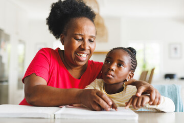 Happy african american grandmother and blind granddaughter reading braille