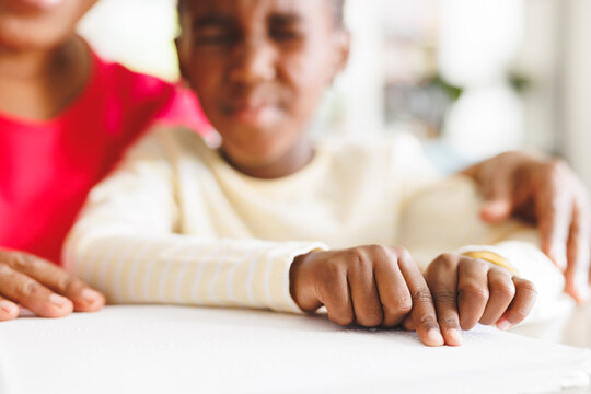 Happy african american grandmother and blind granddaughter reading braille