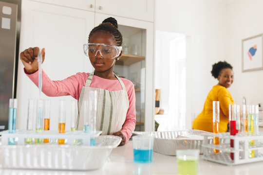 Happy african american grandmother and granddaughter doing chemistry experiments in kitchen
