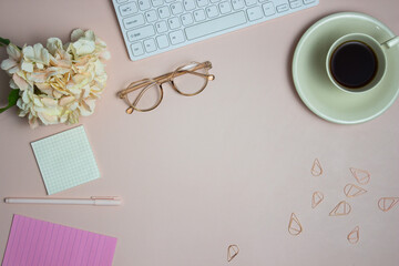 Sweet working space with coffee cup, reading glasses and flower over the pink background.  