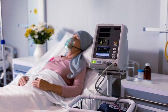 Senior caucasian female cancer patient wearing head scarf in bed with oxygen mask at hospital - Powered by Adobe
