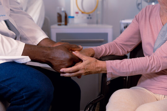 Close up of african american doctor and senior caucasian patient holding hands in hospital