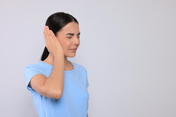 Young woman suffering from ear pain on light grey background. Space for text
