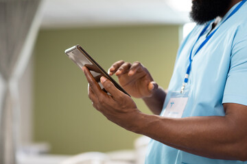 African american male doctor working at hospital, using tablet