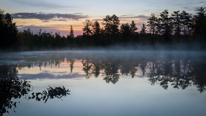 The colors of an autumn sunrise creep into the sky over a secluded Northwoods lake.