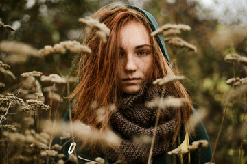 Thoughtful teenage girl with red head standing amidst plants