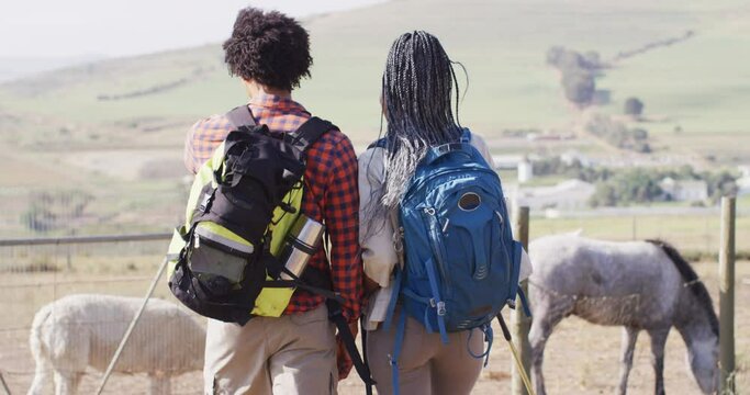 Happy african american couple with backpacks, hiking with trekking poles together, slow motion