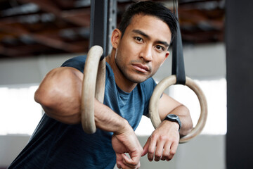 Portrait, gymnastic rings and olympics with a man gymnast hanging on equipment for workout in gym. Face, fitness and exercise with a male athlete training in gymnastics for health or power