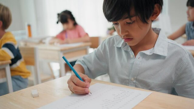 Elementary school students are sitting in the classroom at school and doing final exams in mathematics