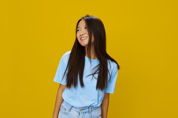 Asian woman smile with teeth hand gestures, signs and symbols on yellow background in blue t-shirt and jeans