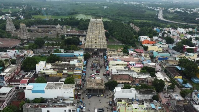 Fly towards the majestic view of Sri Kanchi Kamakshi Amman Temple in Kanchipuram, Tamil Nadu. Wide shot of the temple tower surrounded by agricultural lands and a suburban city.