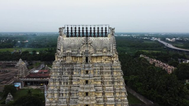 Pull back shot of Sri Kanchi Kamakshi Amman Temple tower surrounded by agricultural lands and suburban city.