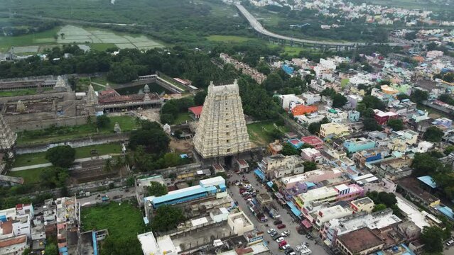 Fly towards a majestic view of Sri Kanchi Kamakshi Amman Temple in Kanchipuram, Tamil Nadu. Wide shot of the temple tower surrounded by agricultural lands and a suburban city.