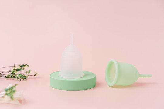 White menstrual cup on green podium and green one on pink background.