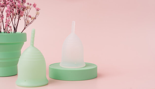 Menstrual cups on green podium next to red dry flowers in power case against pink background.