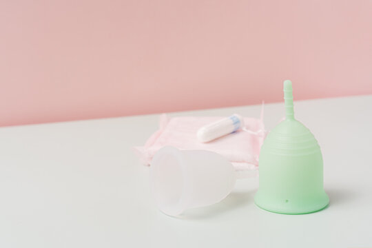 Menstrual cups with pads and tampon on white table against pink background.