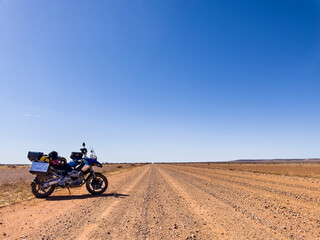 Motorcycle on outback desert road, South Australia, with blue sky.