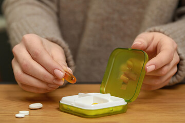 Woman taking pill from plastic box at wooden table, closeup