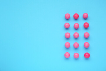 Many bright pink gumballs on light blue background, flat lay. Space for text