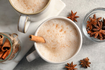 Cups of delicious eggnog with anise and cinnamon on light grey table, flat lay
