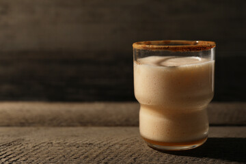 Glass of delicious eggnog on brown textured table. Space for text