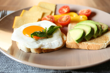 Fototapeta na wymiar Tasty toasts with fried egg, avocado, cheese and vegetables on table, closeup