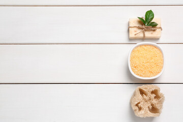 Sea salt, soap bar and loofah on white wooden table, flat lay. Space for text