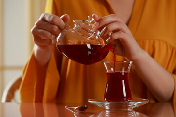 Woman pouring tasty Turkish tea into glass at table, closeup