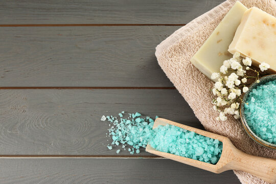 Aromatic sea salt and beautiful flowers on grey wooden table, flat lay. Space for text