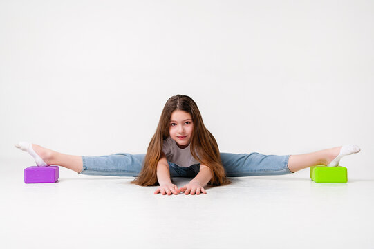 A teenage girl in jeans and a white t-shirt stretches her legs with green and purple styrofoam cubes. White background. The concept of sports, yoga. - Powered by Adobe